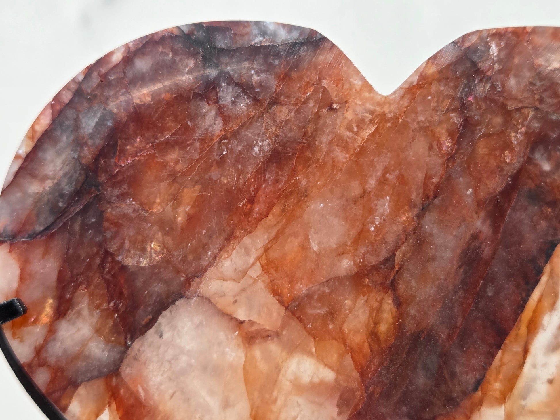 A close-up of a heart-shaped polished stone or crystal with marbled brown, amber, and translucent pinkish tones.