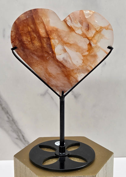 Fire Quartz heart on a black stand, shown against a white wall and marble-patterned background.