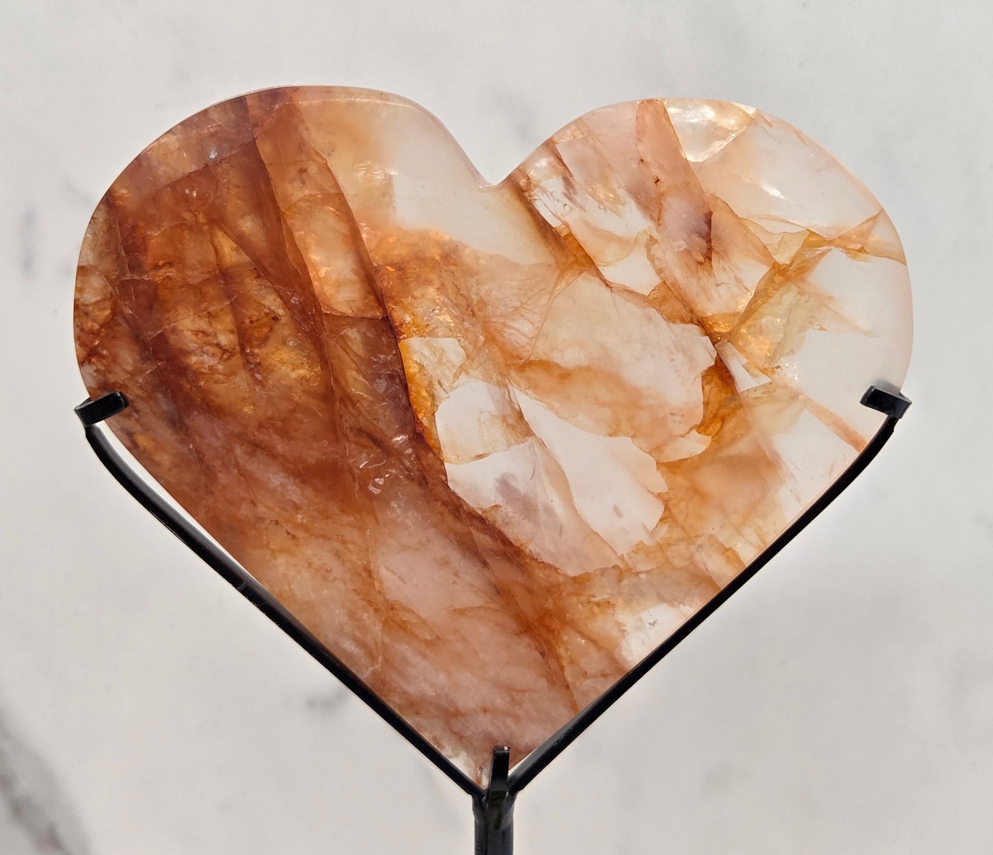 Fire Quartz heart on a black stand, shown against a white wall and marble-patterned background.