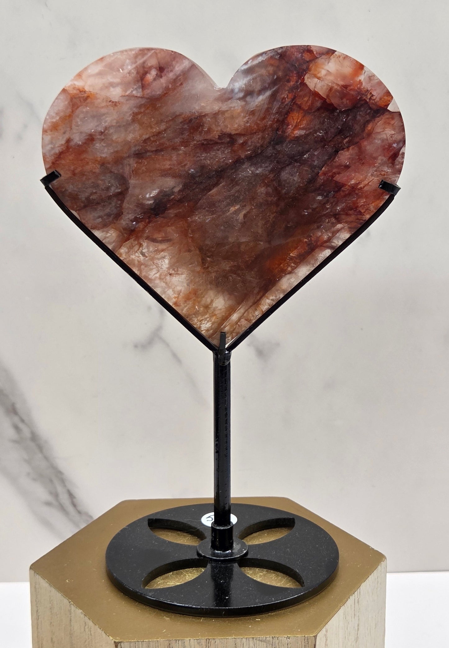 Fire Quartz heart on a black stand, shown against a white wall and marble-patterned background.