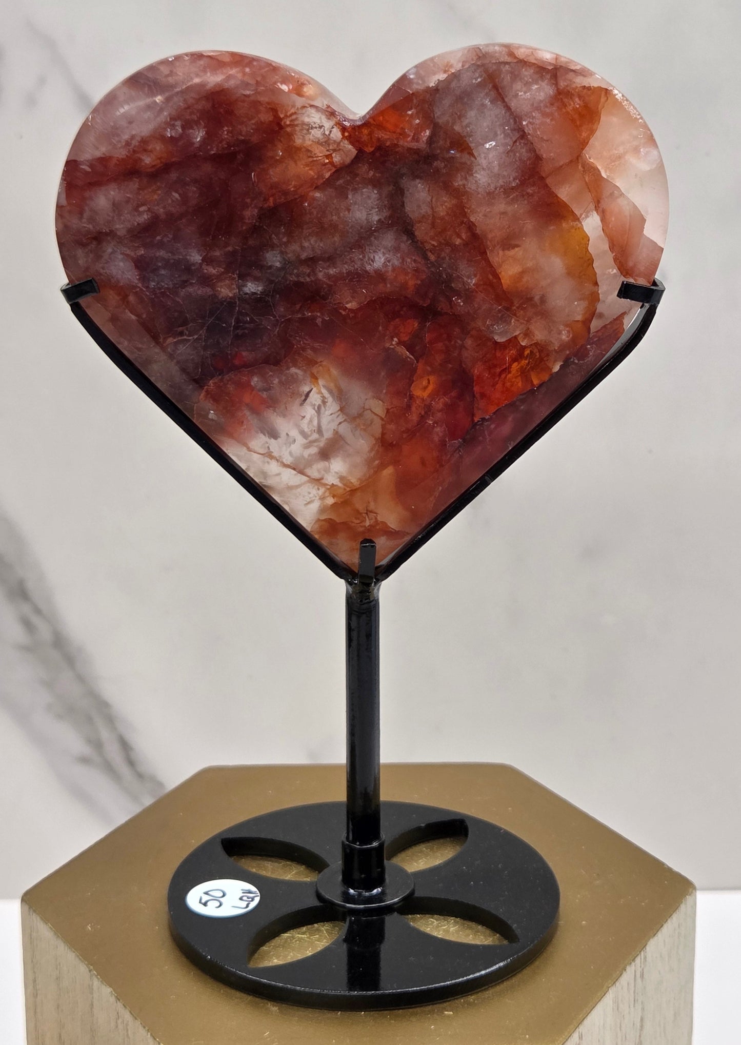 Fire Quartz heart on a black stand, shown against a white wall and marble-patterned background.