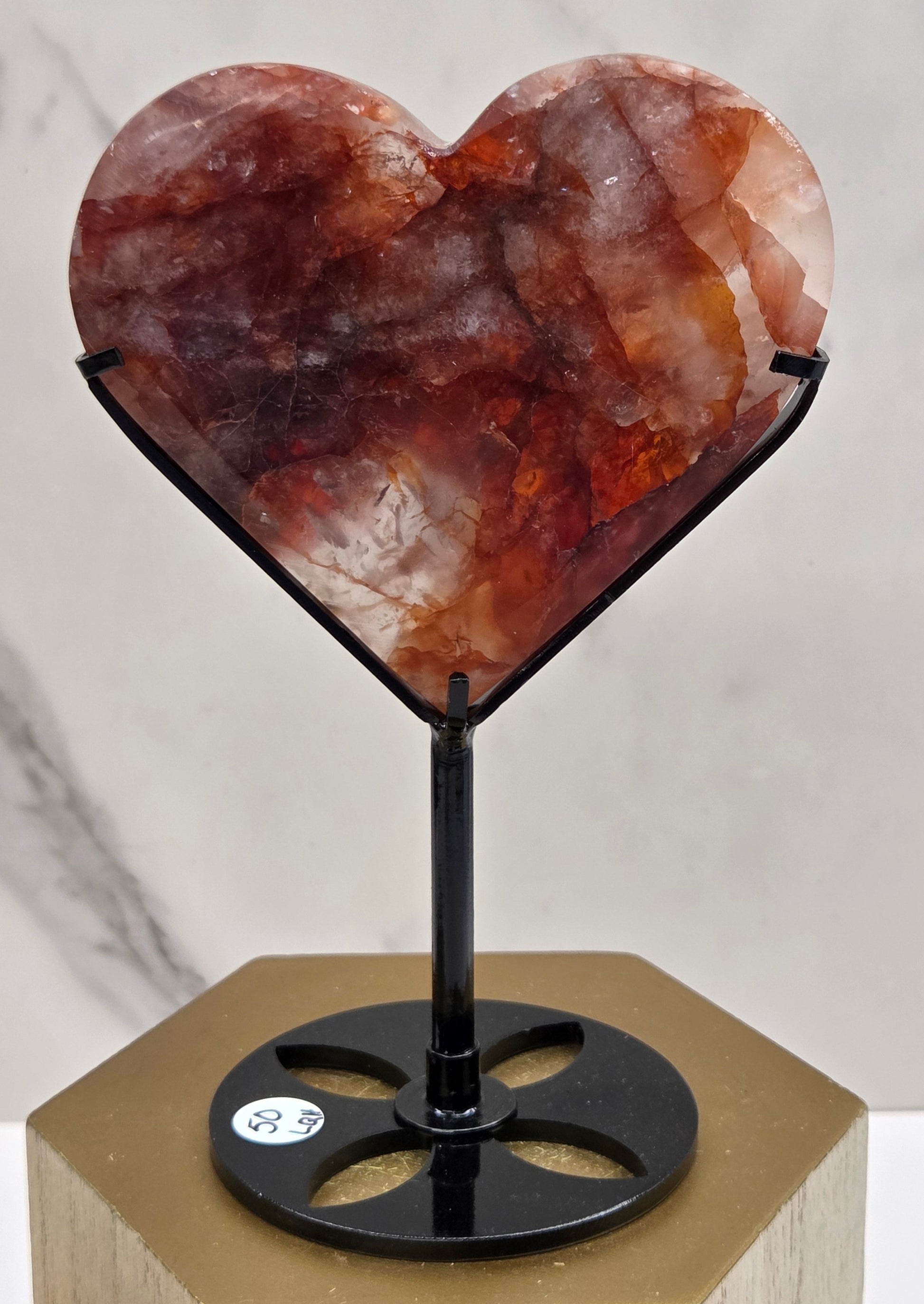 Fire Quartz heart on a black stand, shown against a white wall and marble-patterned background.