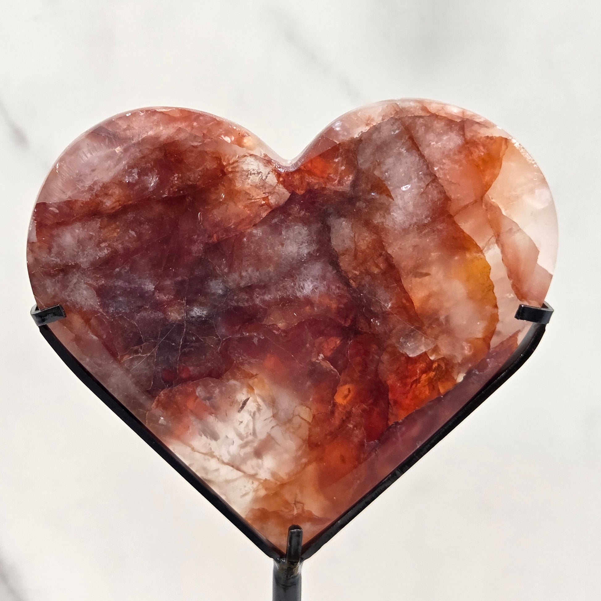 Fire Quartz heart on a black stand, shown against a white wall and marble-patterned background.