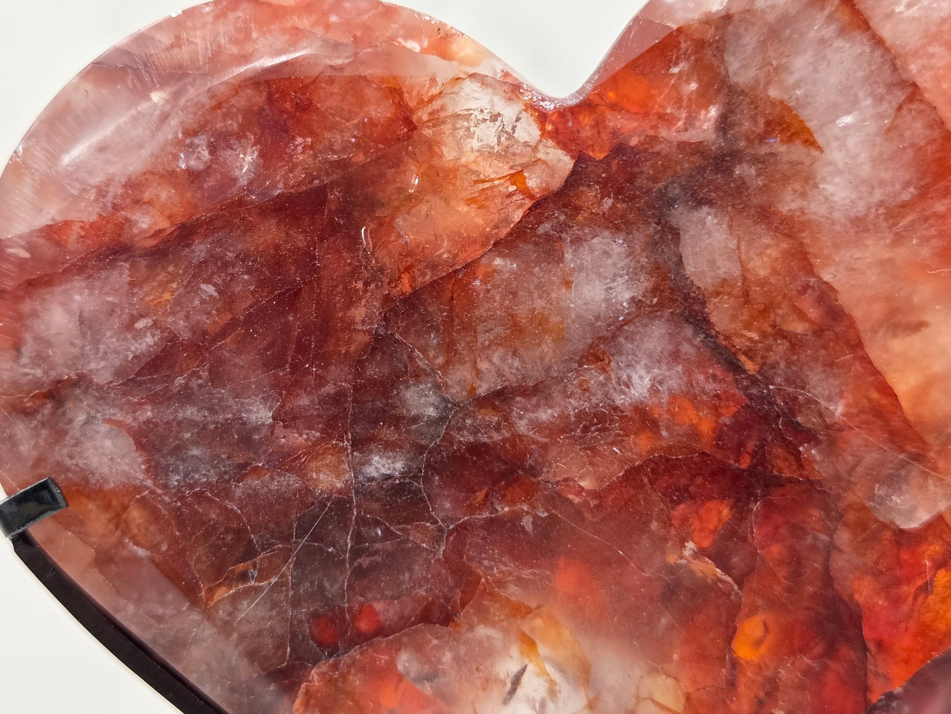 A heart-shaped polished gemstone with a rich color profile of reddish-brown, amber, and translucent white quartz veins, shown close-up against a white background.