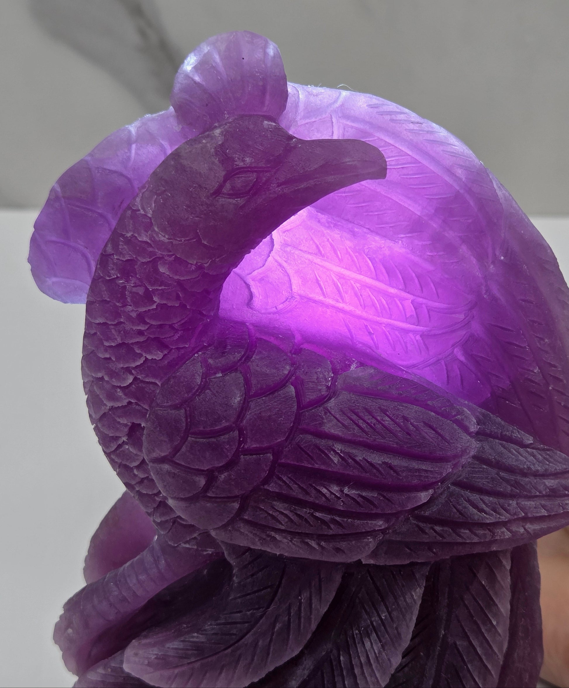 Backlit purple lepidolite phoenix carving on a white background