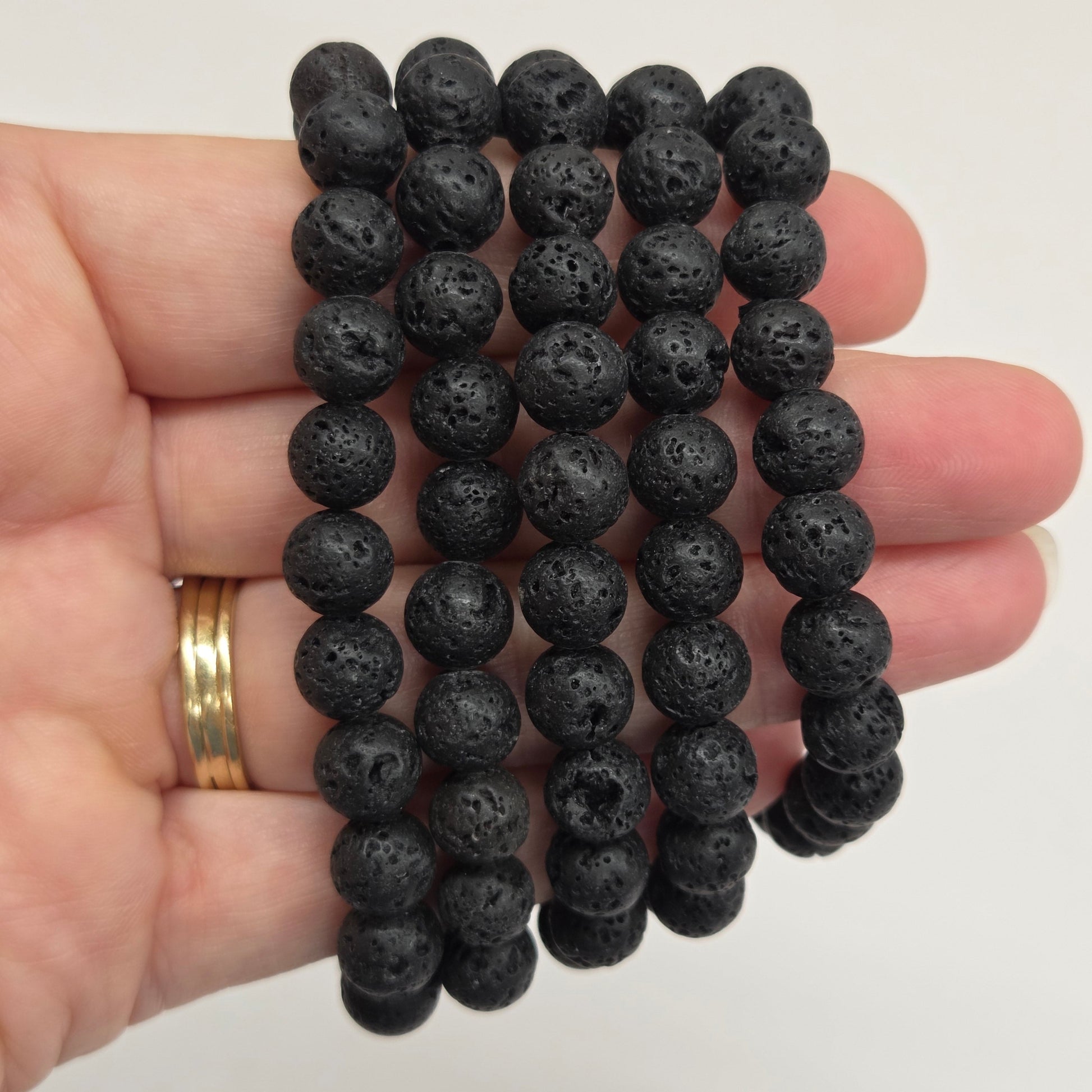 Five black lava stone bead bracelets held in a person's hand against a plain light background.