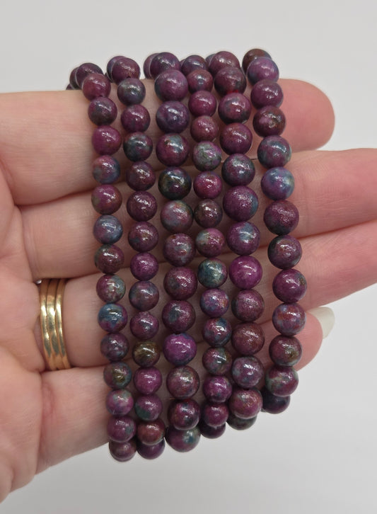 Five strands of small round beads in a dark purple color with iridescent blue and green flashes, held in a person's hand.