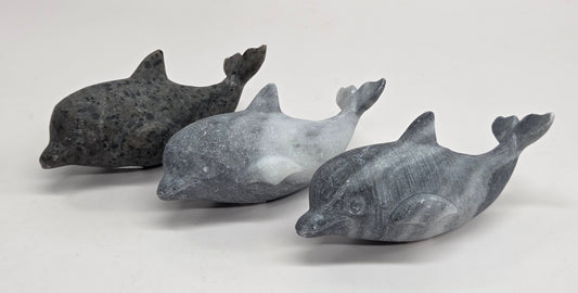 Three small dolphin figurines made from polished stone in dark gray, medium gray, and white, arranged on a light gray surface.