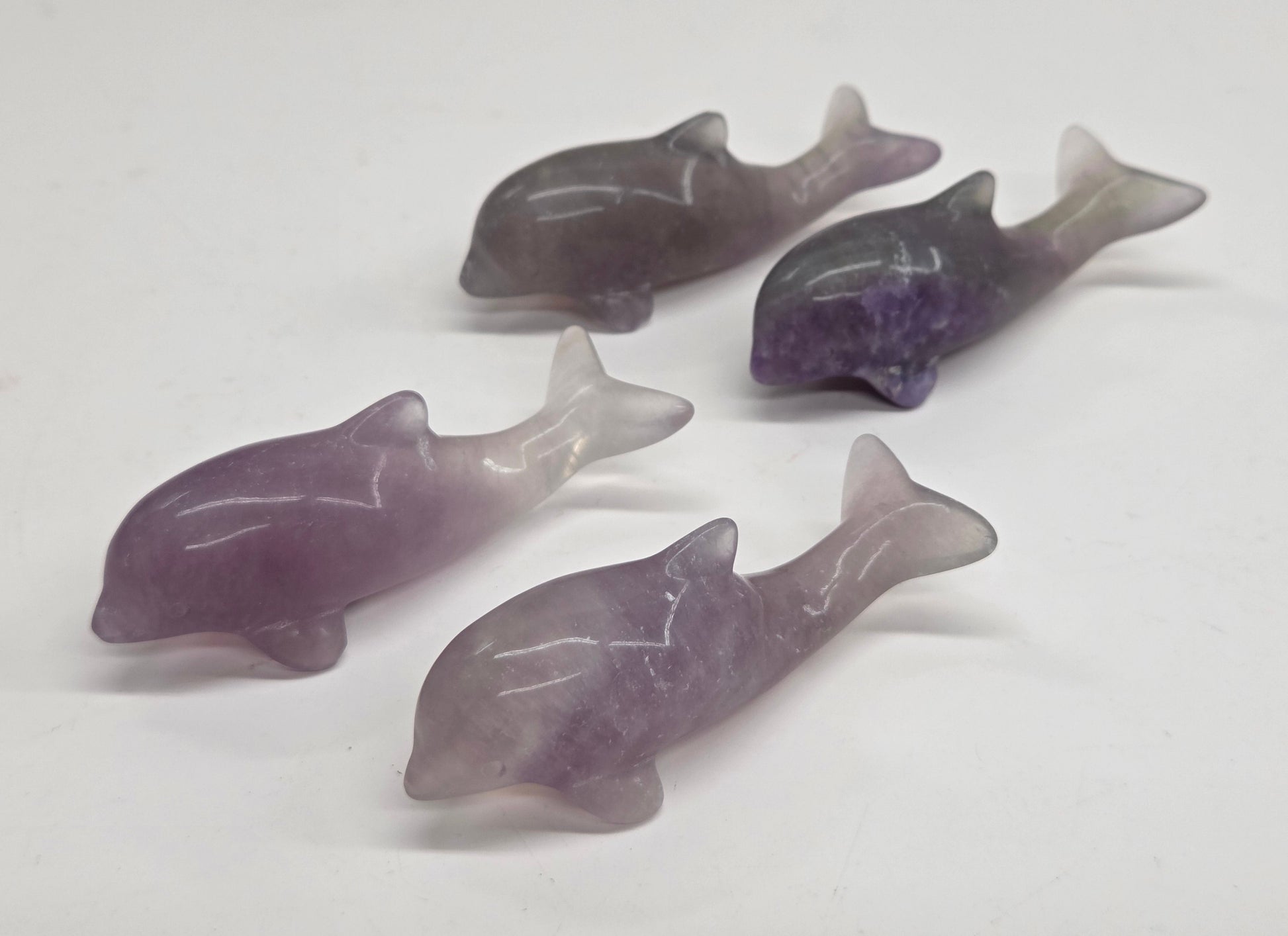 Four small carved dolphin figurines made from purple and gray gradient stone, arranged on a plain white background.