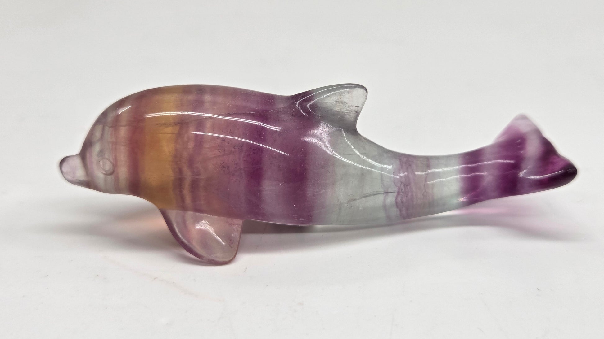 A polished dolphin figurine carved from purple and brown flúorite with white veining, displayed on a plain light gray background.