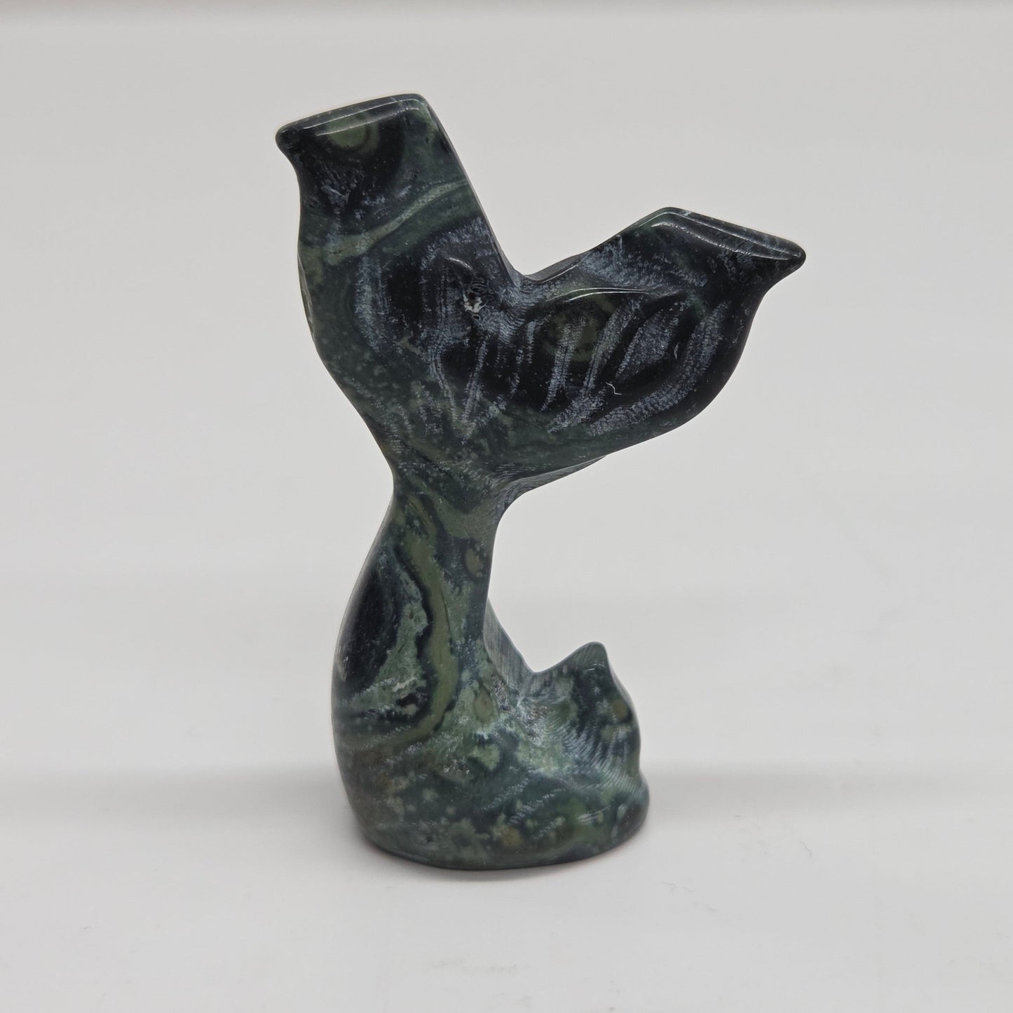 A small carved stone figurine shaped like a mermaid tail, made from kambaba japer, photographed against a plain light background.