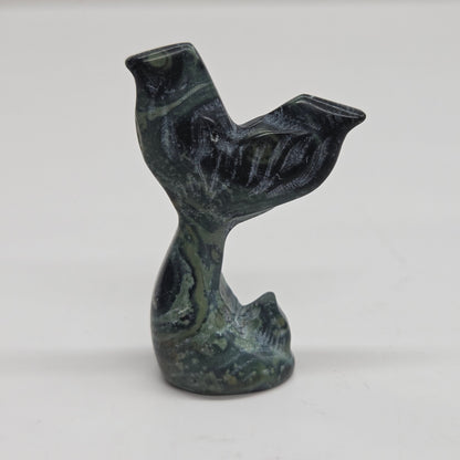 A small carved stone figurine shaped like a mermaid tail, made from kambaba japer, photographed against a plain light background.