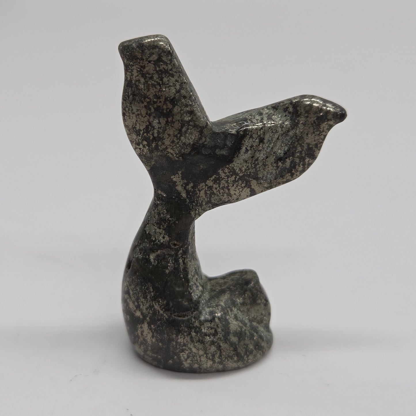 A small carved stone figurine shaped like a mermaid tail, made from pyrite, photographed against a plain light background.