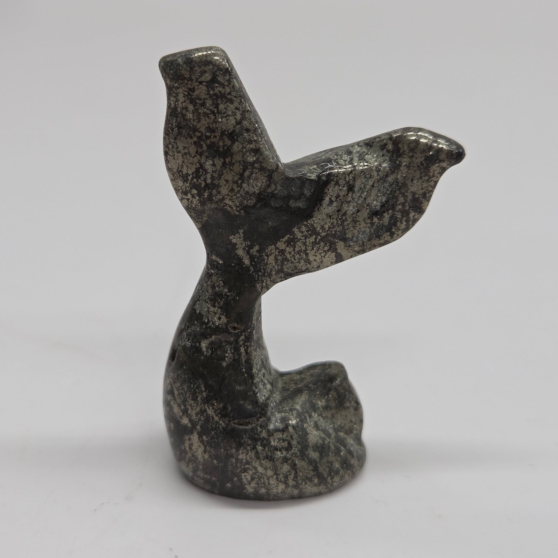 A small carved stone figurine shaped like a mermaid tail, made from pyrite, photographed against a plain light background.