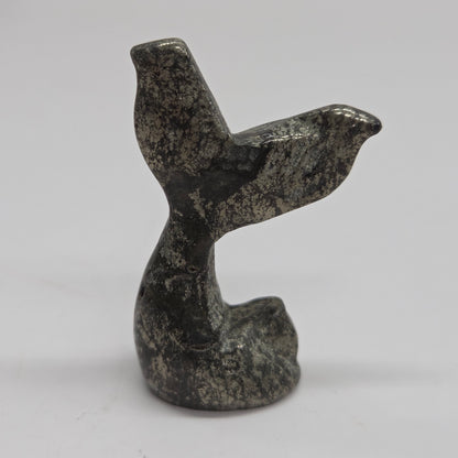 A small carved stone figurine shaped like a mermaid tail, made from pyrite, photographed against a plain light background.
