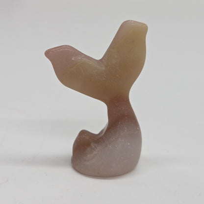 A small carved stone figurine shaped like a mermaid tail, made from banded pink calcite, photographed against a plain light background.