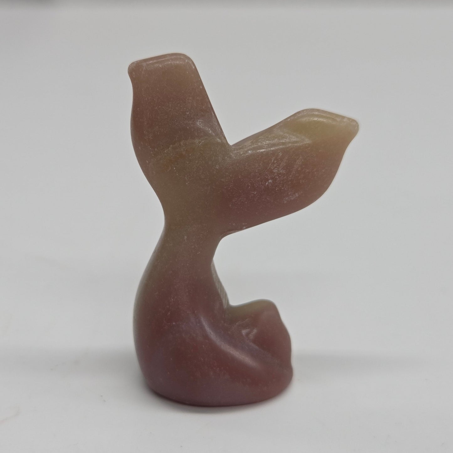 A small carved stone figurine shaped like a mermaid tail, made from banded pink calcite, photographed against a plain light background.