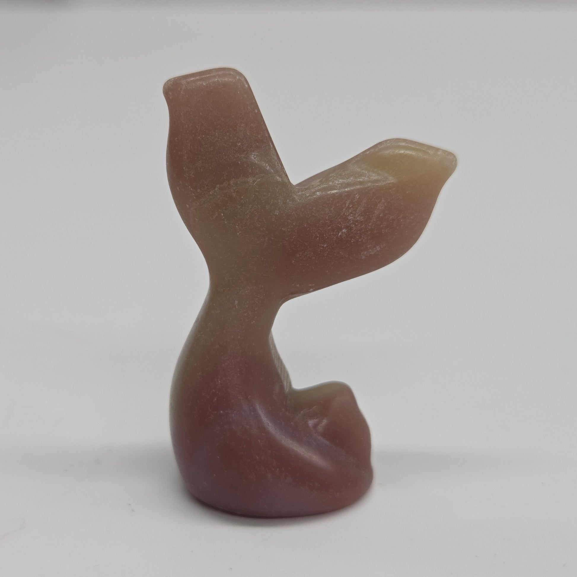A small carved stone figurine shaped like a mermaid tail, made from banded pink calcite, photographed against a plain light background.