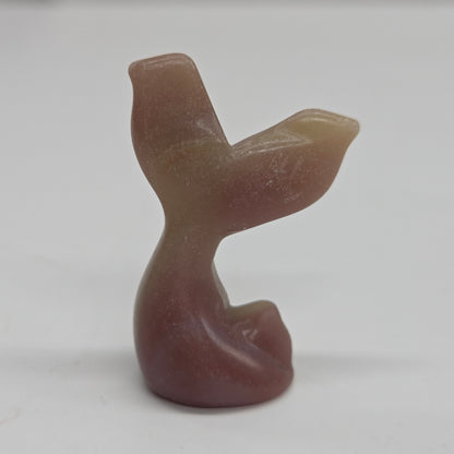 A small carved stone figurine shaped like a mermaid tail, made from banded pink calcite, photographed against a plain light background.