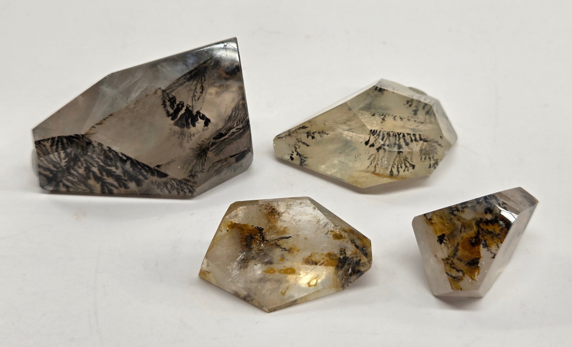 Four rough, faceted natural crystals with internal inclusions, displayed on a plain off-white background.