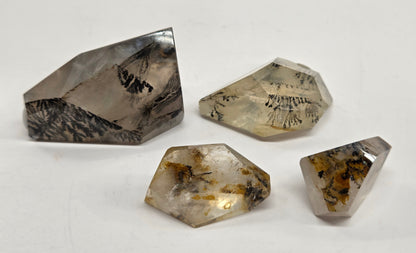 Four rough, faceted natural crystals with internal inclusions, displayed on a plain off-white background.