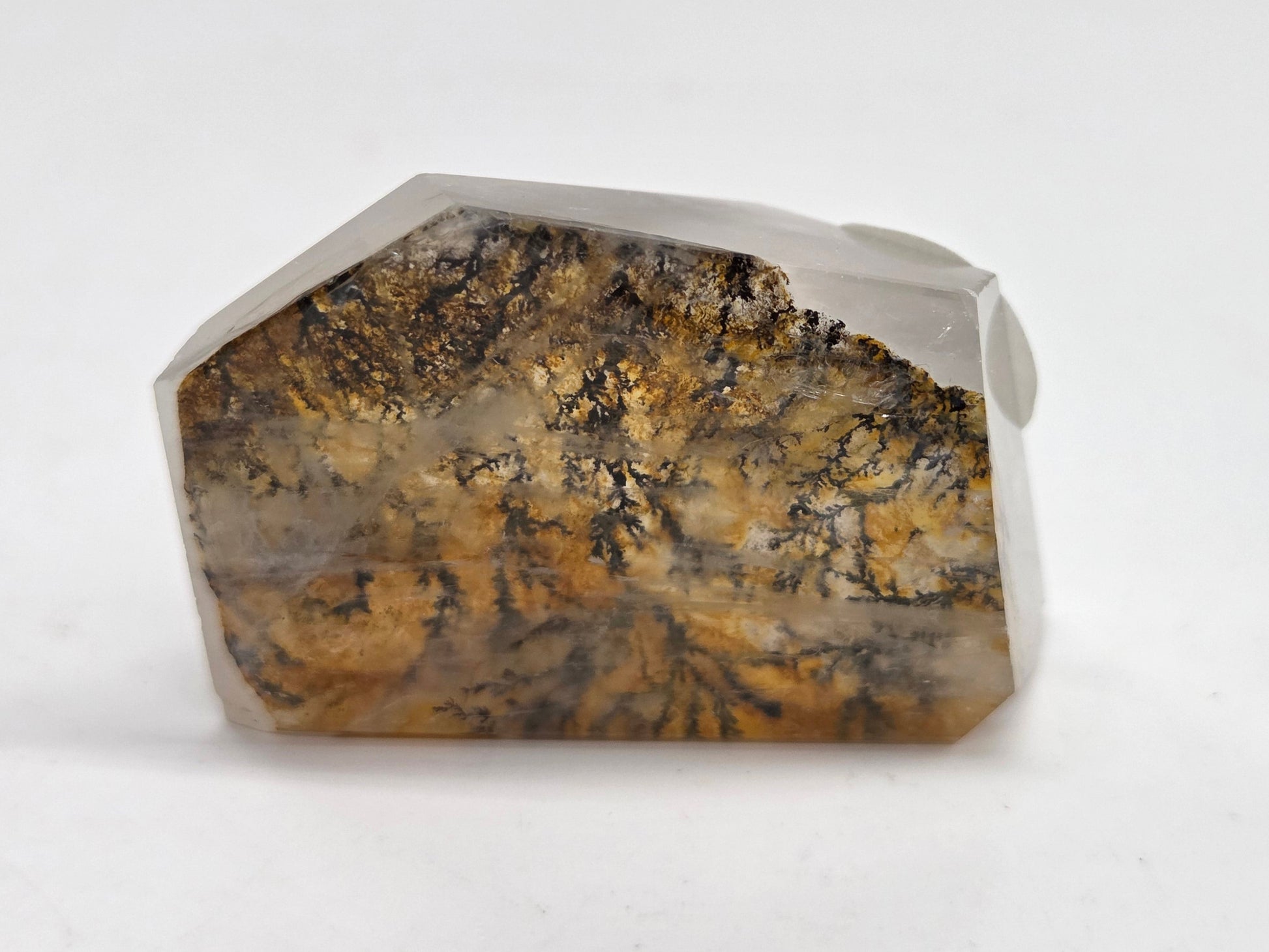 A faceted crystal gemstone with a natural marbled pattern of brown, gold, and black, set in a clear glass or resin base on a white background.