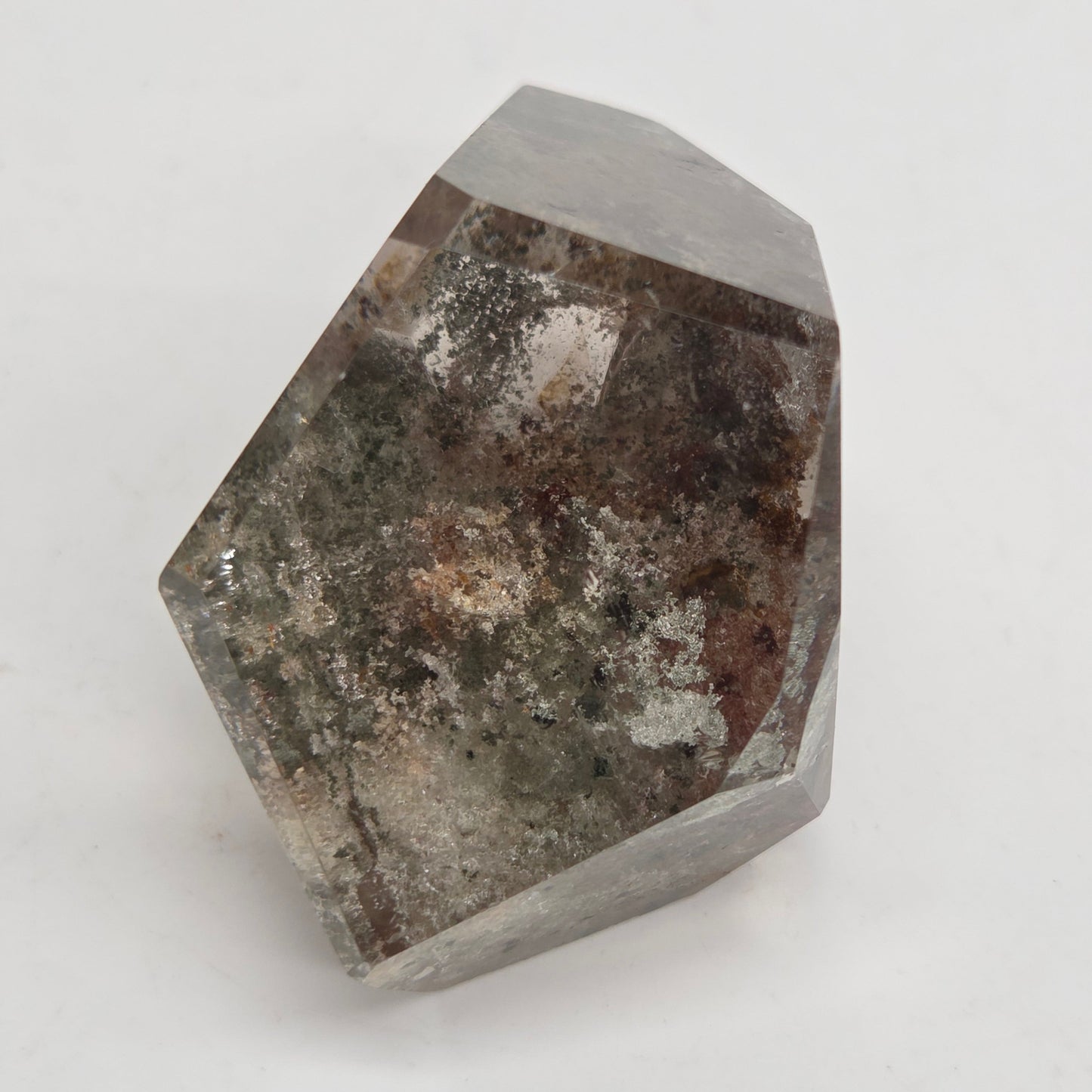 A faceted crystal mineral specimen with a gray base and dark brown, black, and white mineral inclusions, photographed on a plain light gray background.