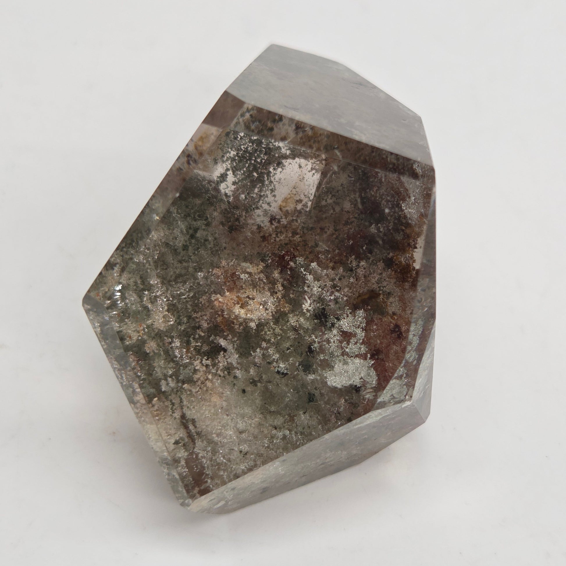 A faceted crystal mineral specimen with a gray base and dark brown, black, and white mineral inclusions, photographed on a plain light gray background.