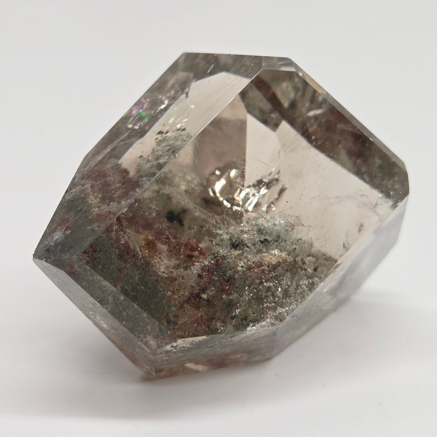 A faceted clear gemstone with internal inclusions and a metallic silver reflection, photographed on a plain light gray background.