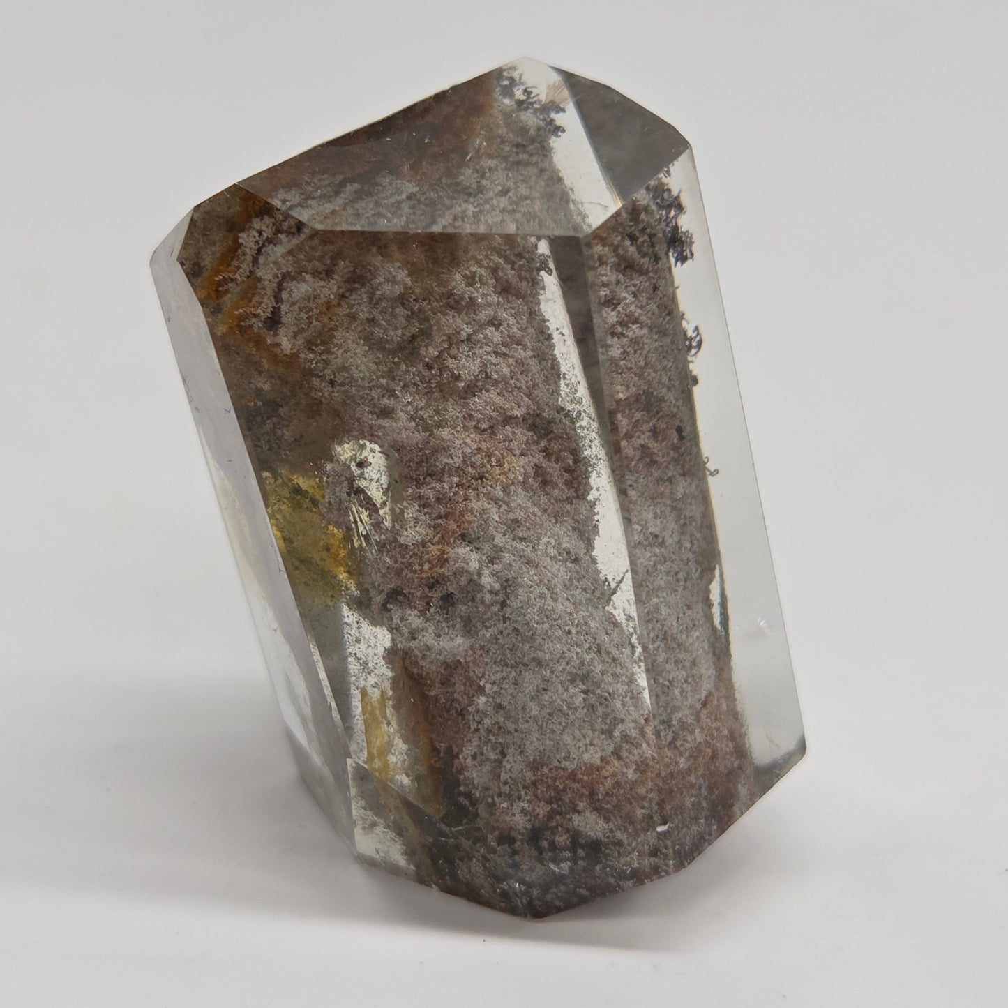 A faceted clear crystal mineral specimen with prominent brown and gray matrix inclusions, photographed on a neutral light gray background.