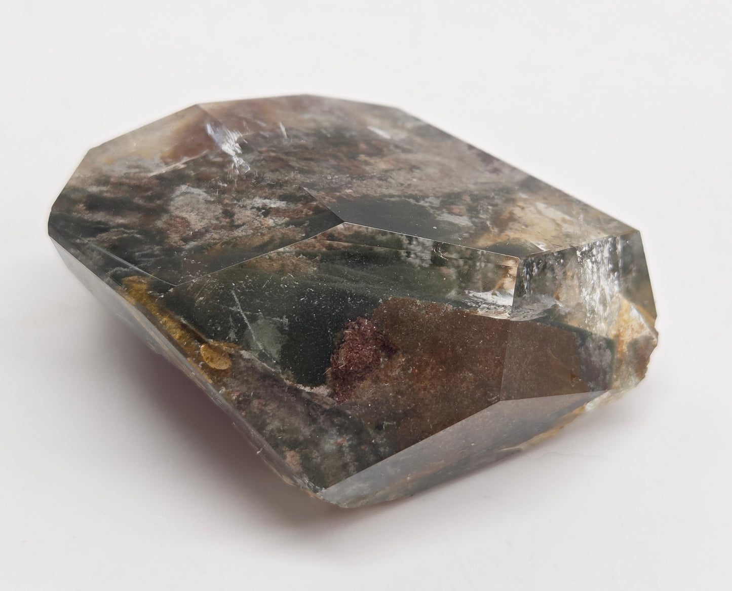 A faceted raw gemstone with a dark gray and black base, showing natural inclusions and internal brown and reddish-brown pockets, photographed on a plain white background.