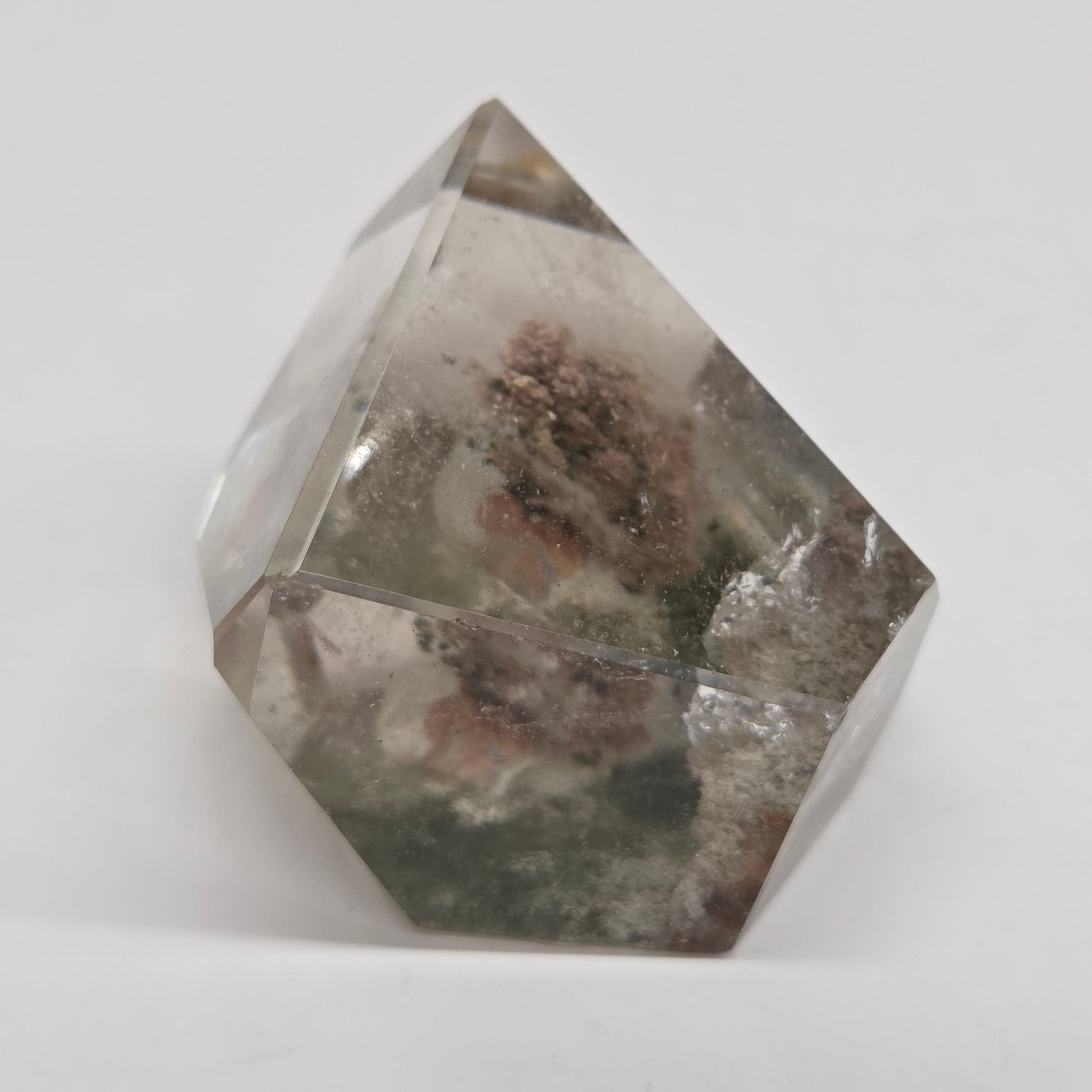 A faceted clear crystal or glass-like geometric ornament with internal cloudy inclusions and a small brownish textured area near the center, photographed on a plain light background.