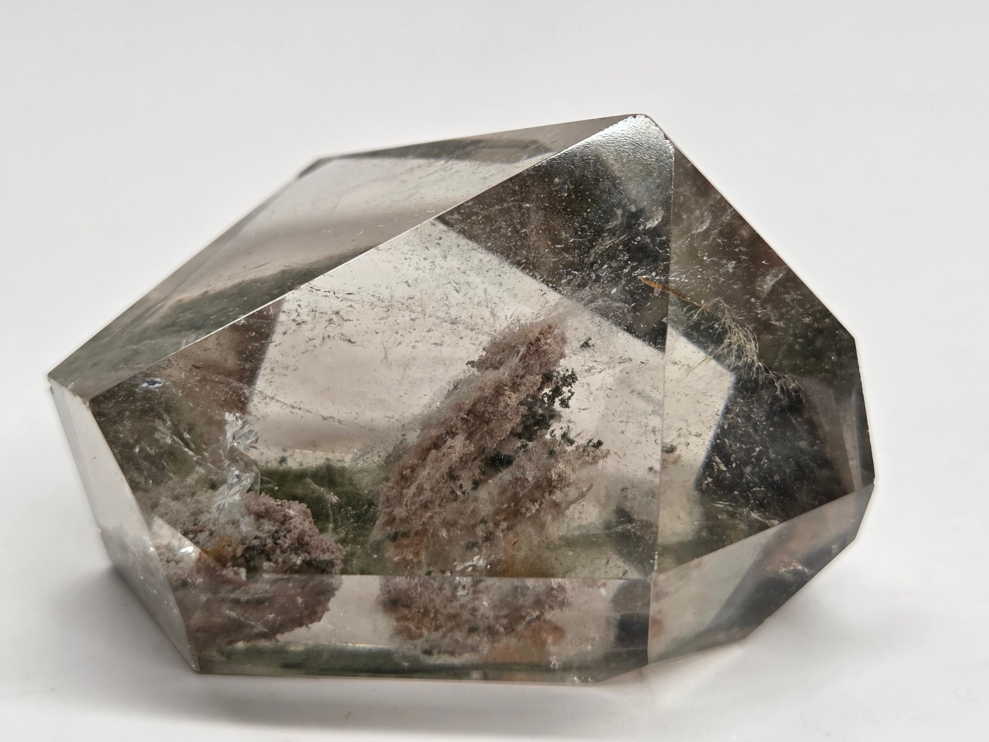 A faceted clear crystal or gemstone with internal inclusions and a smoky gray-brown center, photographed on a plain light background.