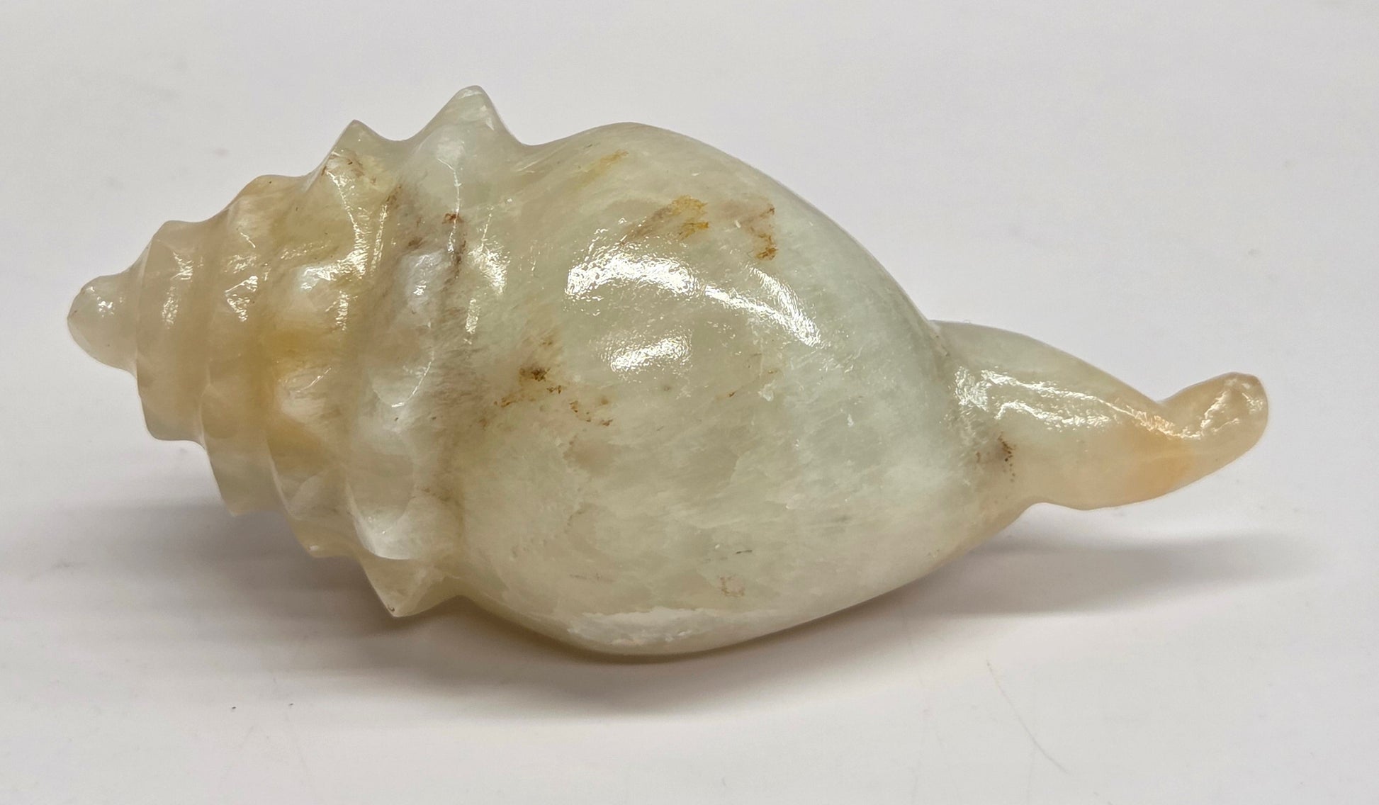 A carved stone shell figurine with a glossy finish, featuring natural beige and cream tones with subtle brownish inclusions, displayed on a plain white surface.