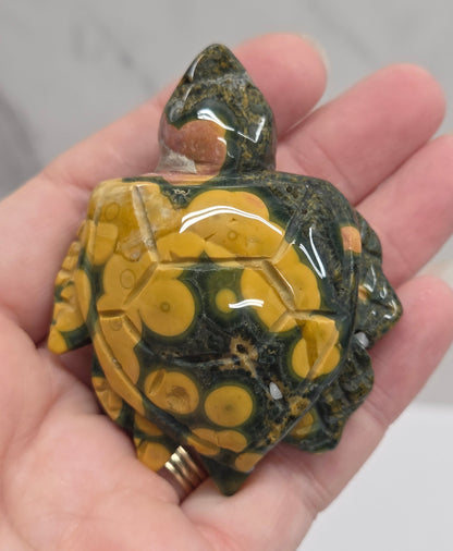 A hand holding a polished green and yellow spotted stone turtle figurine.