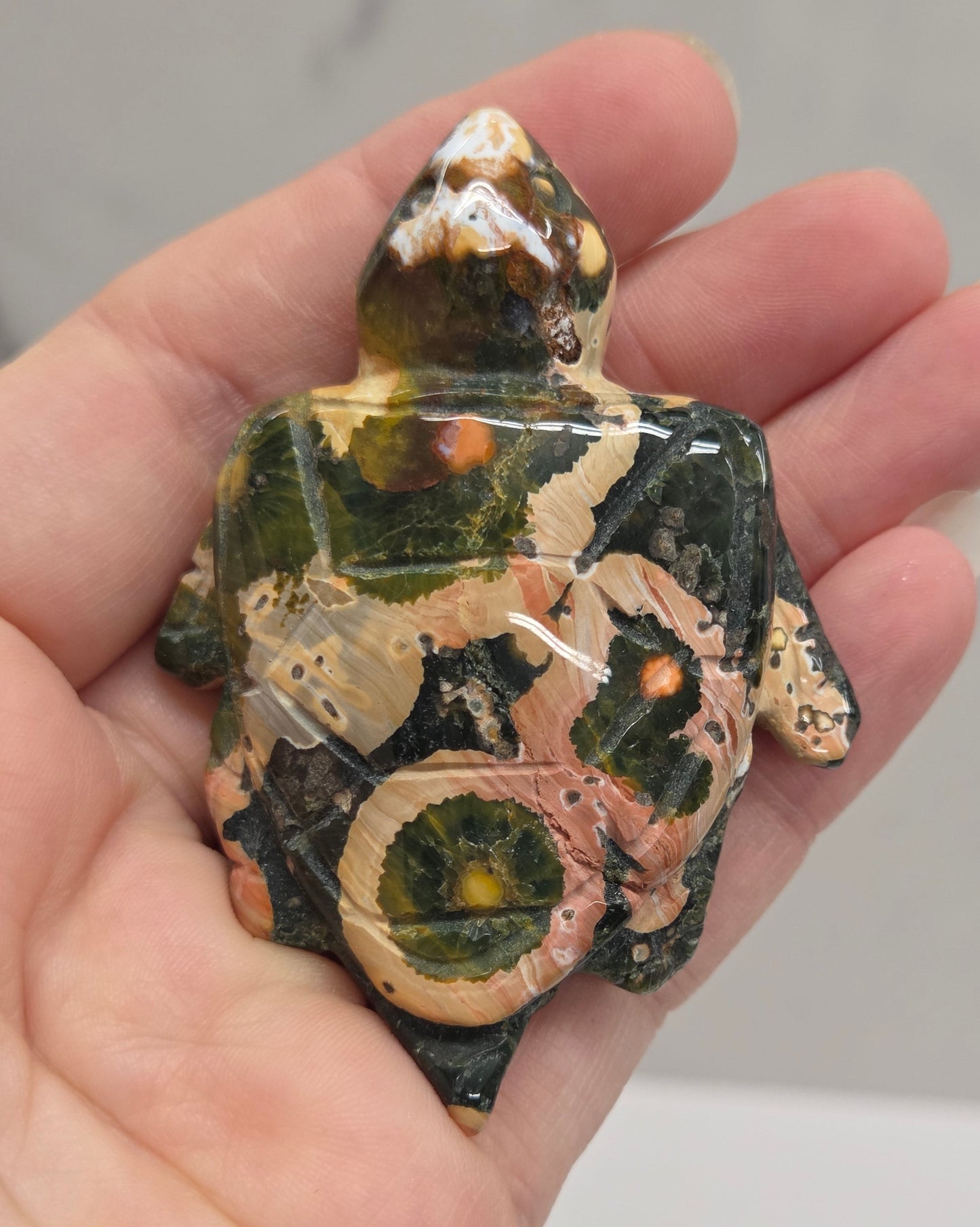 A hand holding a small decorative turtle figurine made from polished stone or glass, showing a marbled pattern of green, beige, and brown.