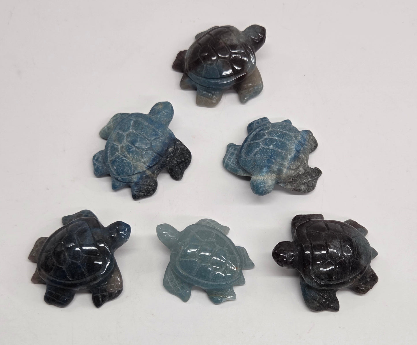 Five carved sea turtle figurines made from blue-gray jasper stone, arranged on a plain off-white surface.