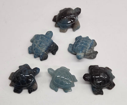 Five carved sea turtle figurines made from blue-gray jasper stone, arranged on a plain off-white surface.