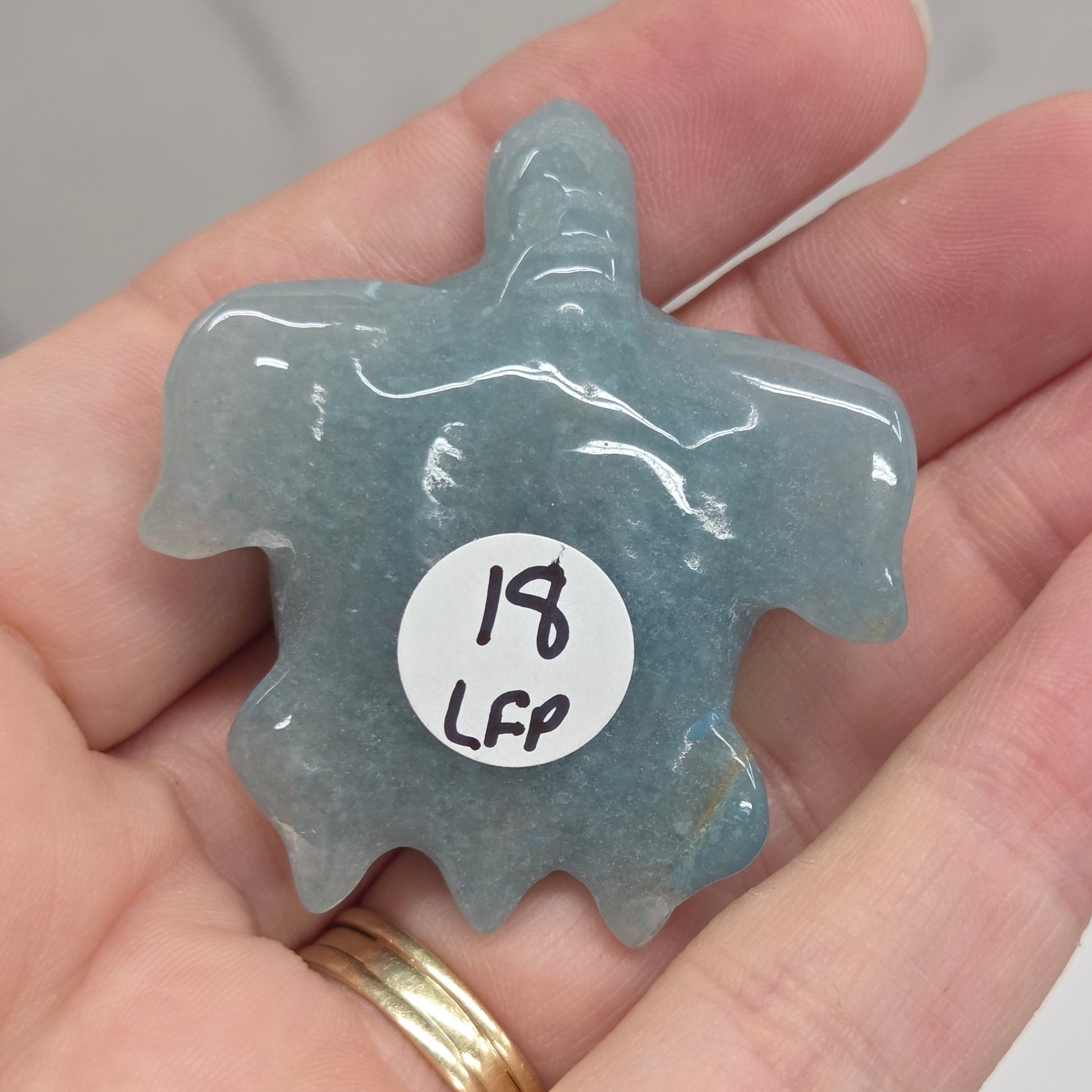 A hand holding a small, irregularly shaped translucent blue-gray stone or crystal with a white circular sticker that reads '192 LHS'.