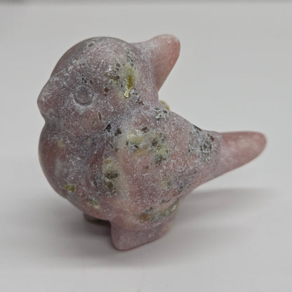 A small carved bird figurine made from pinkish stone with natural speckled green and gray inclusions, standing on a plain light background.