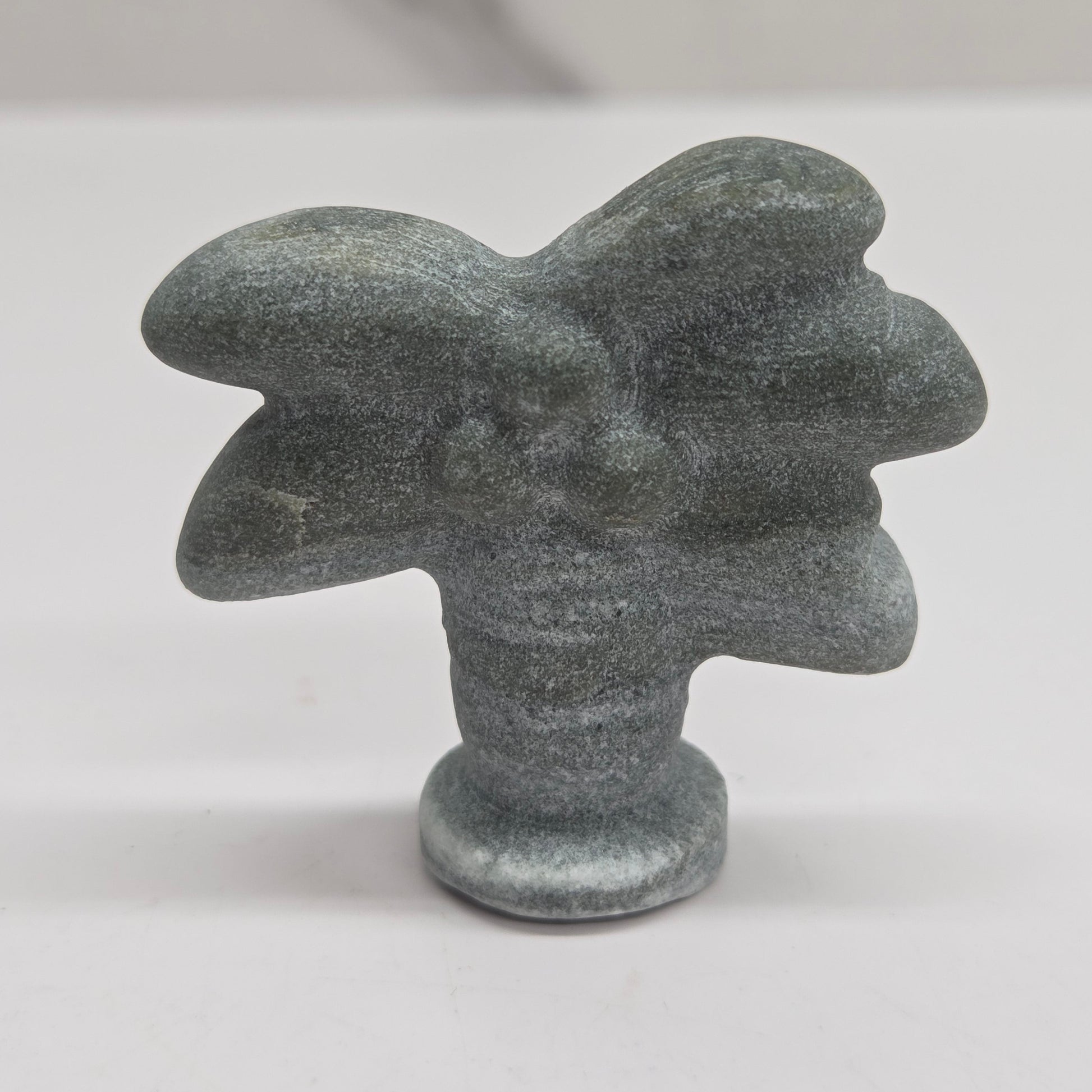 A small abstract sculptural object with a rounded organic shape and a short cylindrical base, shown on a plain light background.
