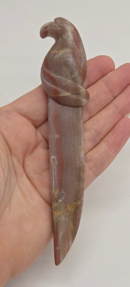 A small carved stone knife with a curved handle and a pointed blade, held in a person's hand against a plain light background.