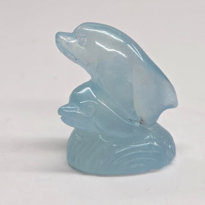 A small light blue carved figurine of two dolphins on a plain white background.