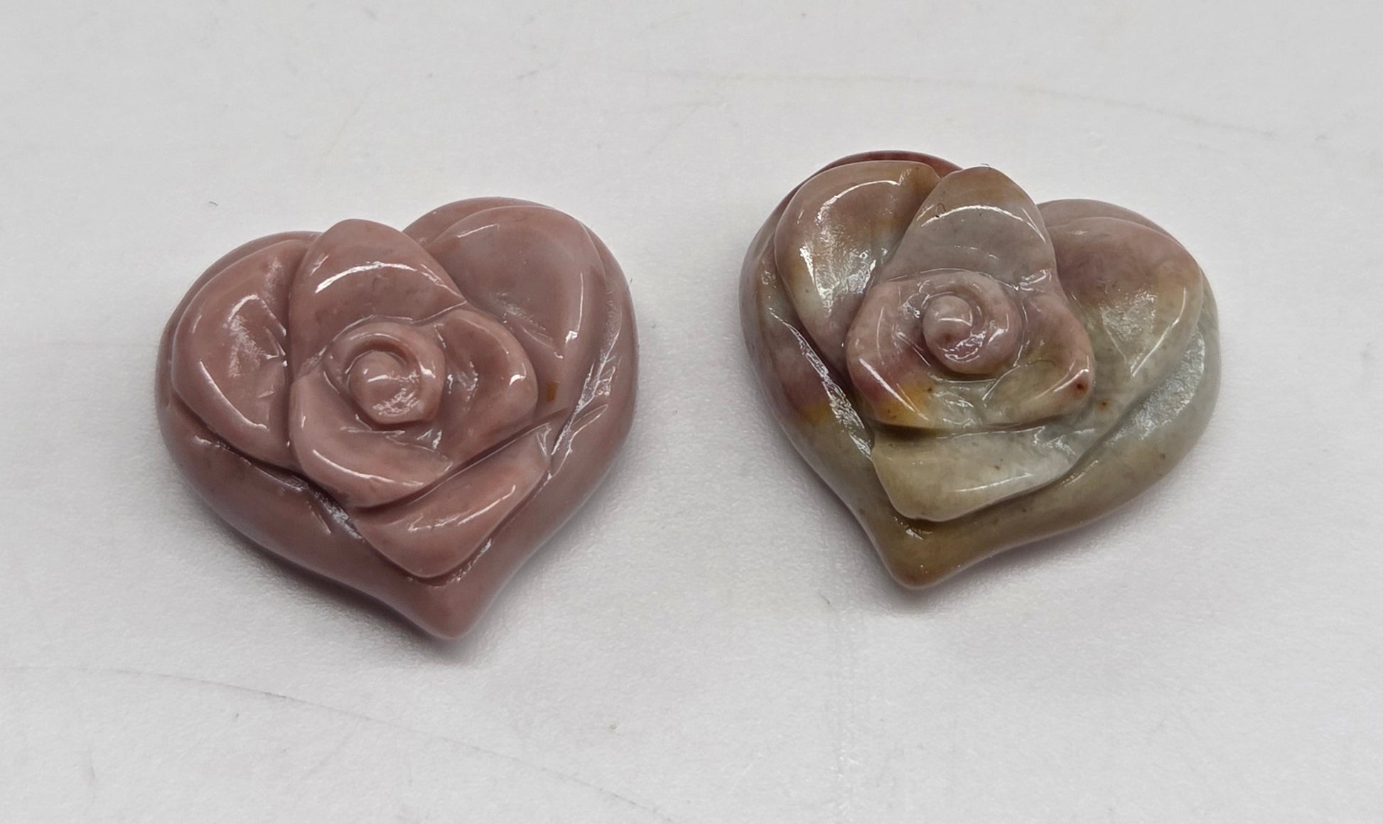 Two small heart-shaped rose-shaped beads on a plain light gray background.