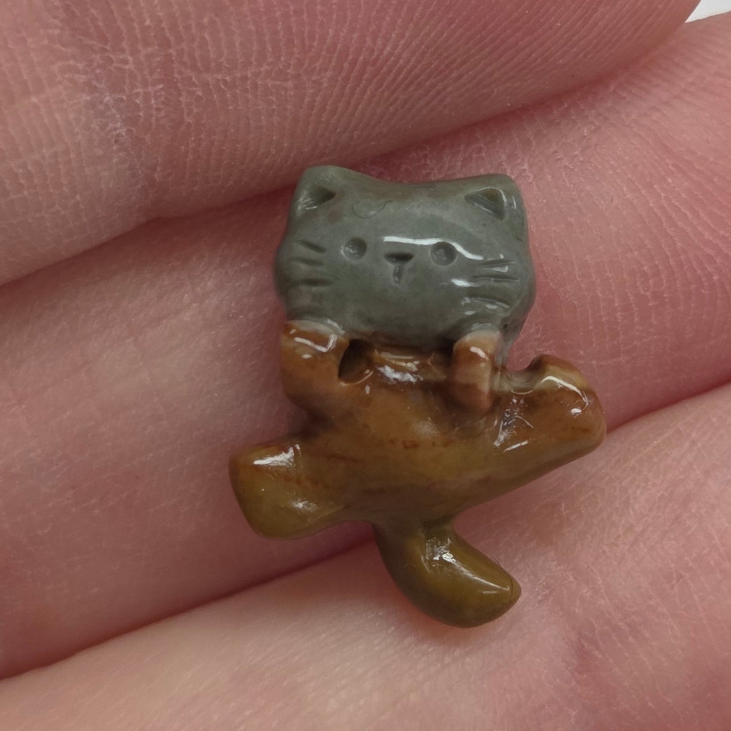 A small ceramic figurine of a cat, displayed on a person's fingers against a white background.