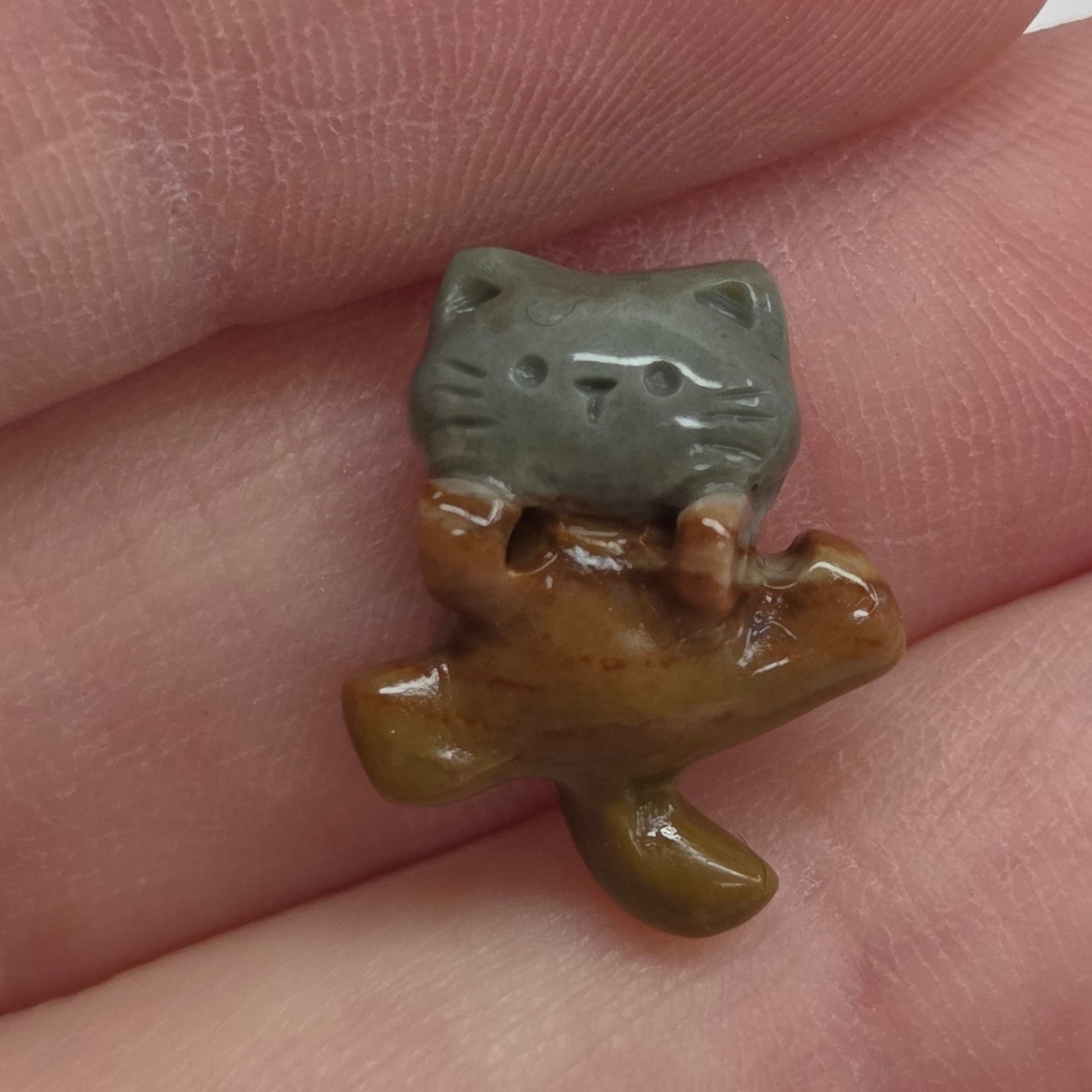 A small ceramic figurine of a cat, displayed on a person's fingers against a white background.