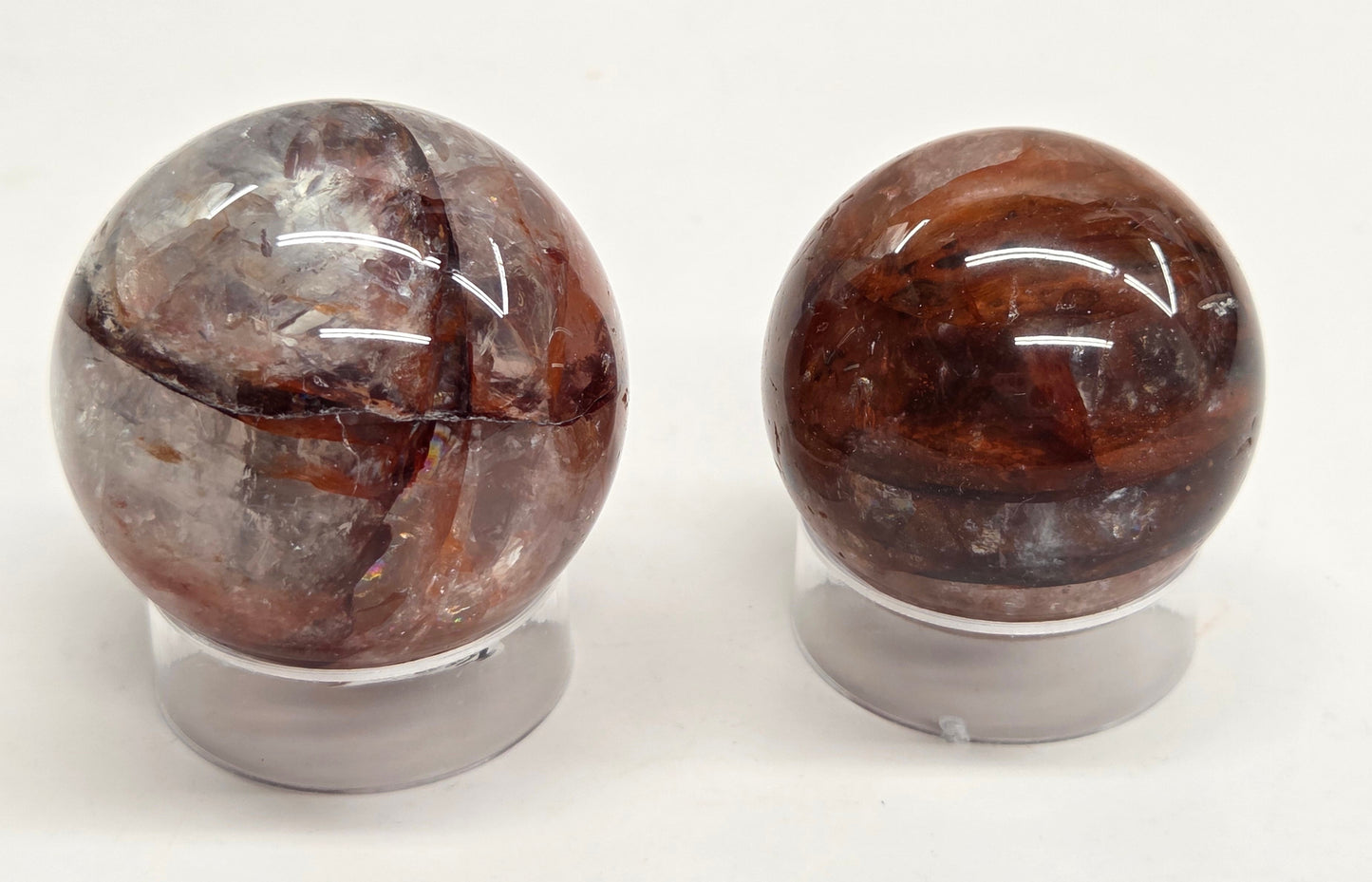 Two polished brown and smoky transparent crystal spheres displayed on clear acrylic stands against a plain white background.
