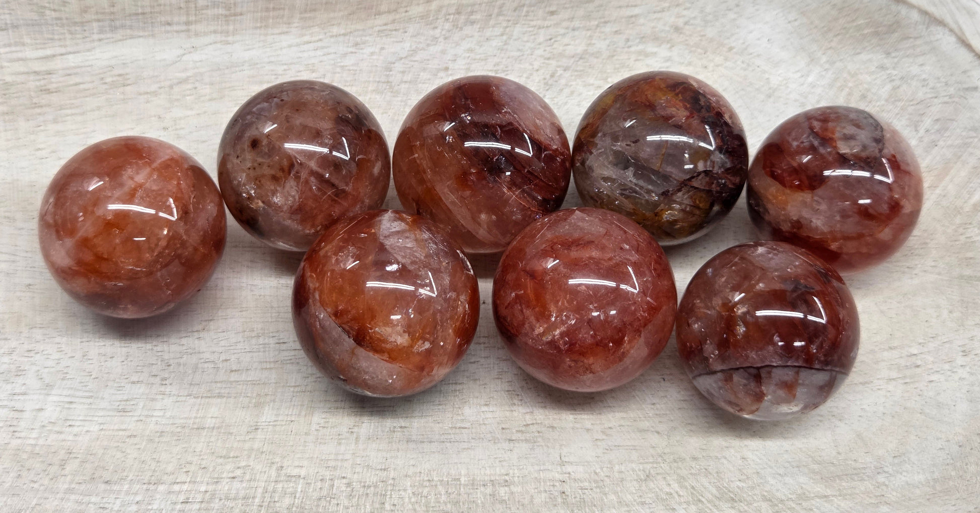Eight polished round gemstone beads in a warm reddish-brown and smoky gray color, arranged on a light beige textured tray.