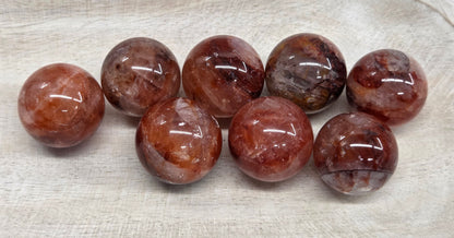 Eight polished round gemstone beads in a warm reddish-brown and smoky gray color, arranged on a light beige textured tray.