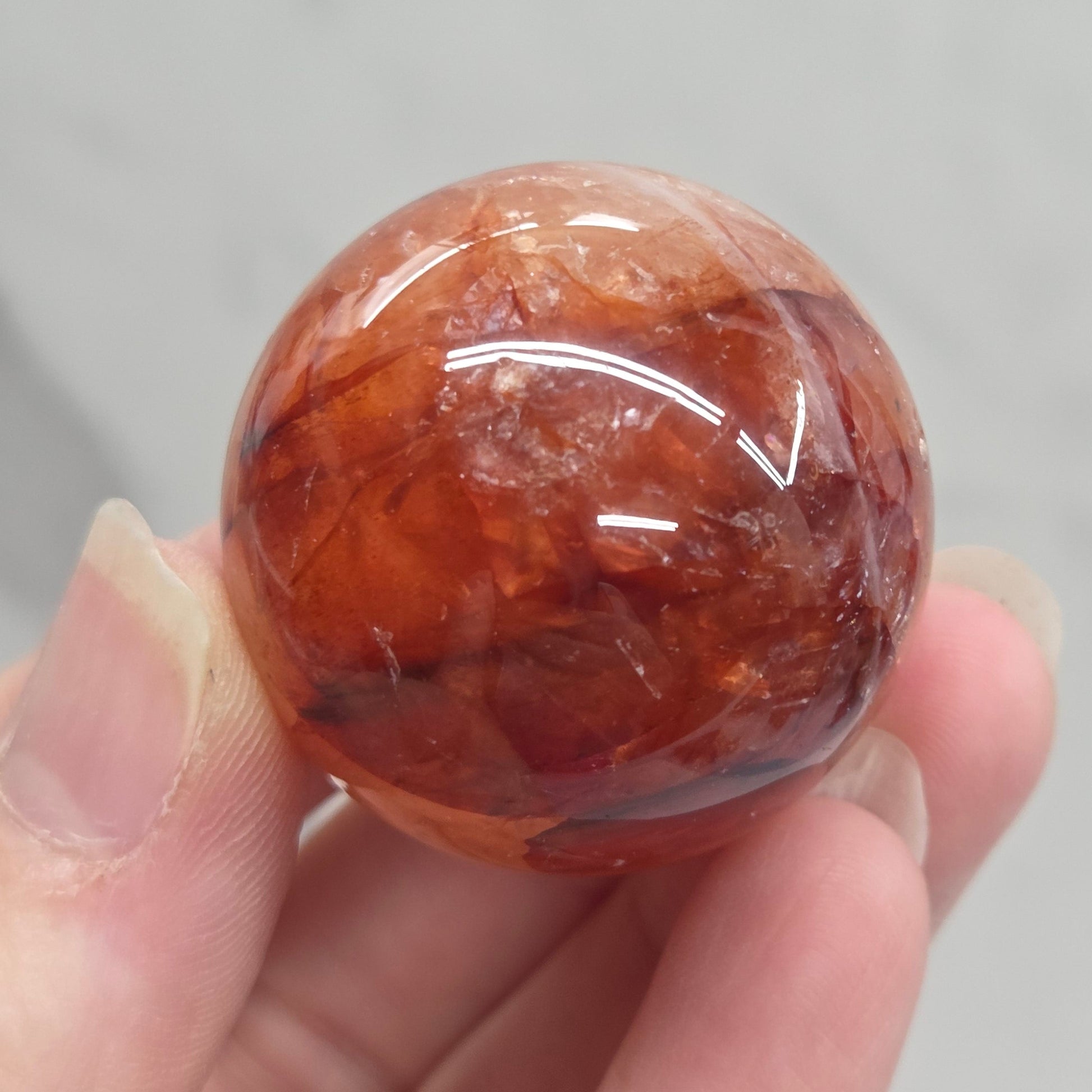 A hand holding a polished round orange-brown stone or crystal sphere against a light gray marble-like background.